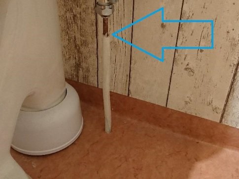 En toalettstol med synligt plast- och kopparrör; en pil pekar på potentiellt läckage mellan materialet.