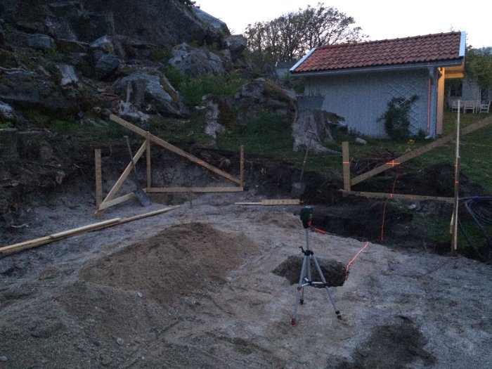 En grävd grop med sand och en laserutrustning som hjälper till vid byggprojekt i skymningen.