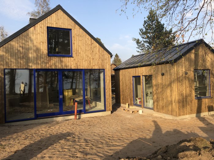 Nybyggt hus med kebony character panel på fasaden, stora fönster och blåa fönsterkarmar under solig himmel.