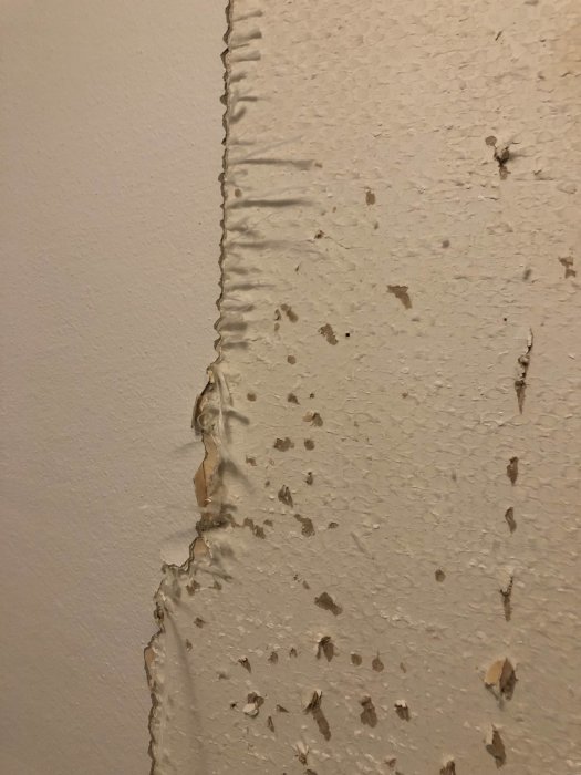 Vägg med delvis borttagen tapet och synliga rester, i behov av renovering.