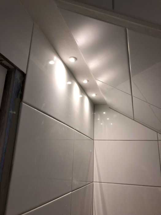 Nyinstallerade spotlights i ett vitt kaklat badrumstak och dusch med lysande belysning.