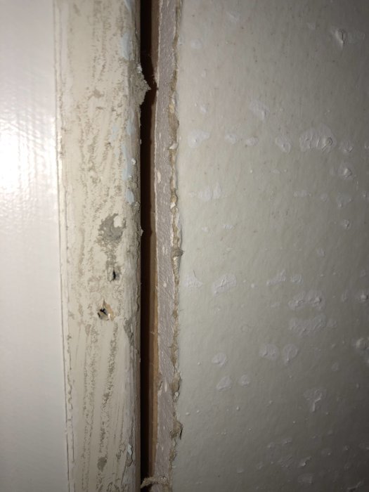 Skadad väggyta med stort spackelarbete behövande reparation, synlig gipskant och ojämn struktur.