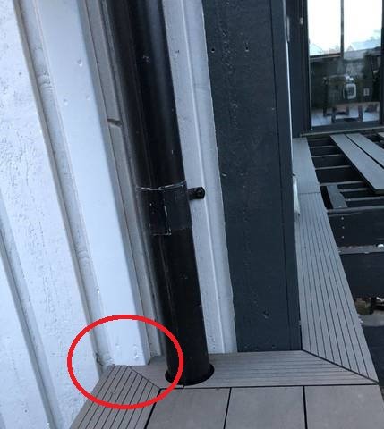 Vattenrör längs en byggnads sida med en markerad del där röret möter altangolvet, vilket kan indikera ett byggnadsfel eller skada.