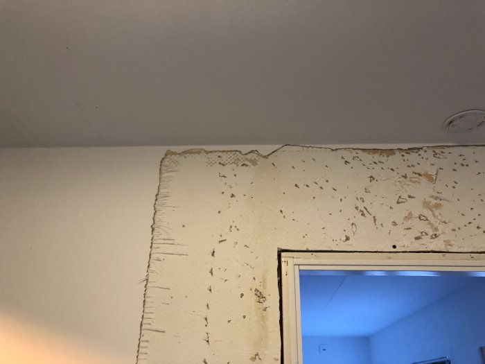 Delvis borttagen glasfiberväv på vägg nära taket med synliga skador och lossning.