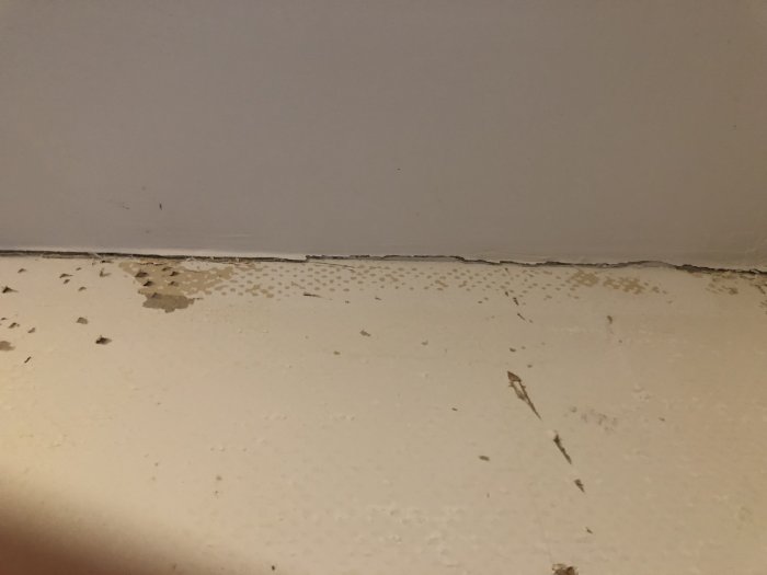 Vägg möter tak där glasfiberväven skalar av och lossnar vid hörnet, med synliga spår av spackel.