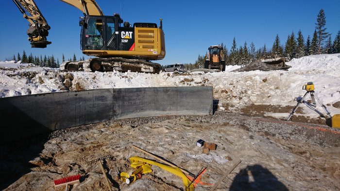 En grävmaskin och en hjullastare på ett snöigt bygge med verktyg och mätinstrument i förgrunden.