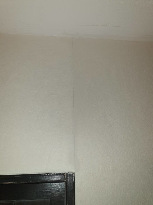 Nymålad vägg med osynliga hörnskarvar precis efter uppsättning ovanför svart dörrkarm.