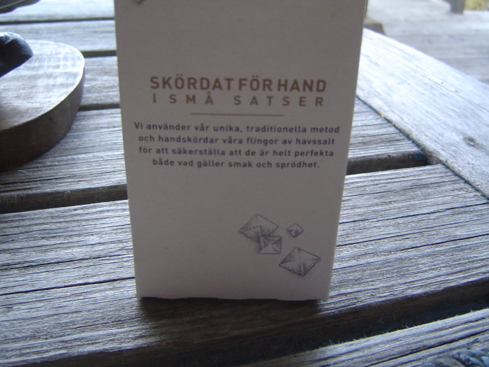 Informationskort som förklarar handskörd av havssalt ligger på ett träbord.