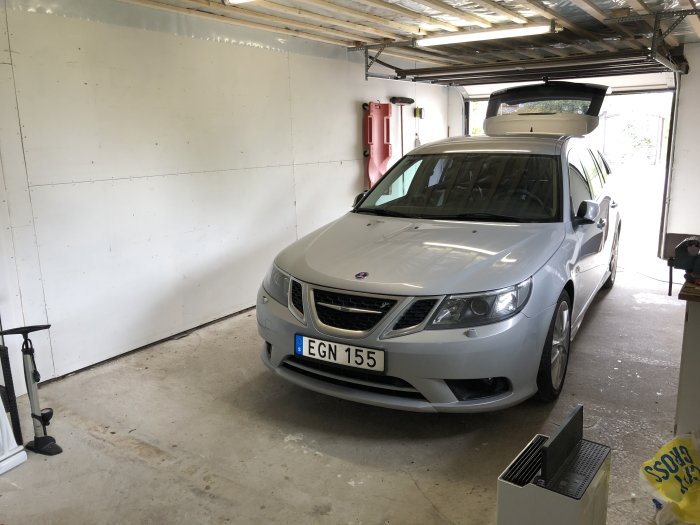 Bil parkerad i renoverad garageinteriör med borttagen köksinredning och plats för nya hyllor.