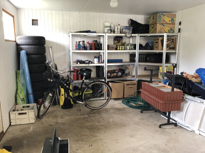Garage med nyinhandlade hyllor, cykel, däckstapel och diverse föremål.