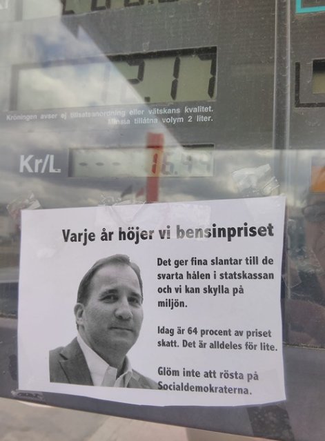 En lapp med text och bild på en politiker klistrad på en bensinpump, med reflekterande siffror i bakgrunden.