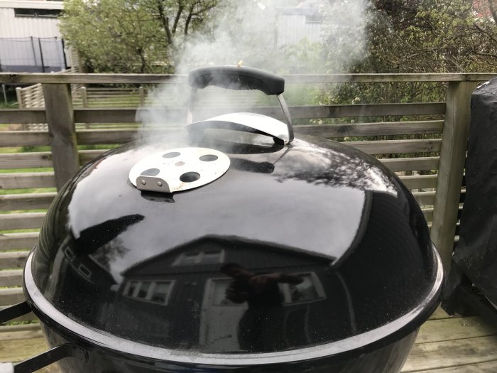 Rökig grill på veranda som används för att röka lax, med reflektion av hus.