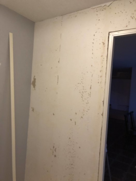 Vägg med spår av tapet och skador som behöver spacklas före rullspackling.