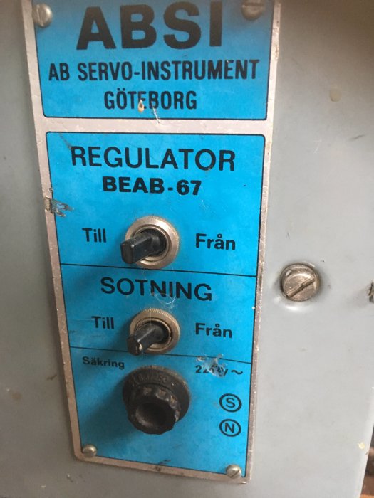 Gammal och trasig regulatorpanel med texten "ABSI AB SERVO-INSTRUMENT GÖTEBORG" och inställningsknappar.