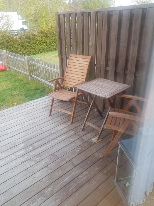 Två trästolar och ett träbord på en träaltan, vilket är de enda utemöblerna som familjen lyckats skaffa.