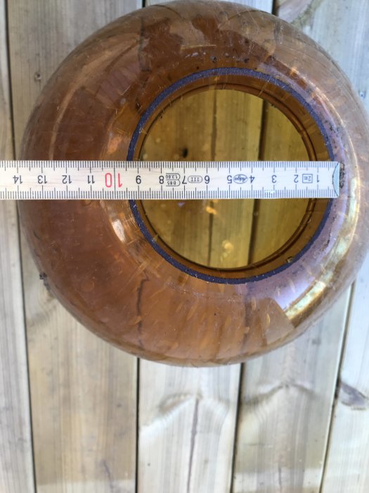 Mätmått placerat över en transparent lampa för att mäta dess innerdiameter mot en träbakgrund.