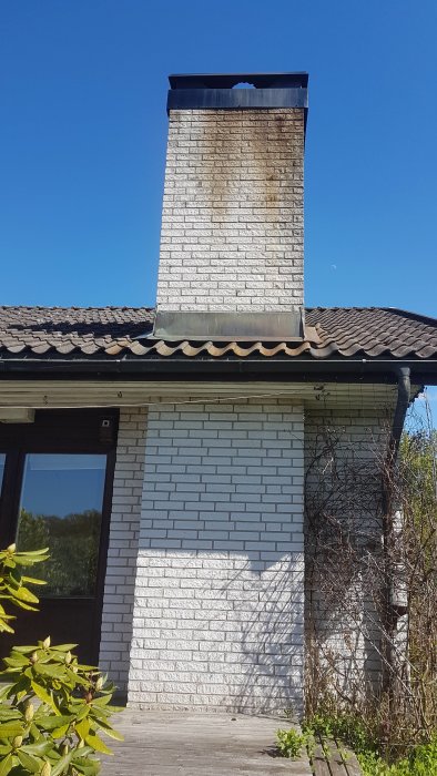 Sotig mexitegelskorsten på ett hus med halmtak mot en klarblå himmel.