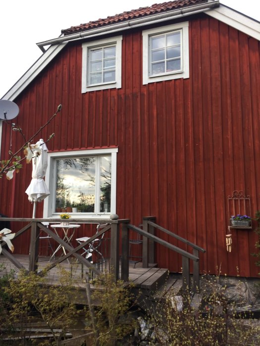 Traditionellt rött hus med vita fönsterkarmar, ett större fönster utan spröjs på bottenvåning och ett mindre fönster med spröjs på ovanvåning.