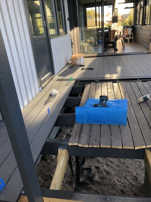 Pågående altanbygge med blöta reglar och en improviserad lösning, verktyg och material syns.