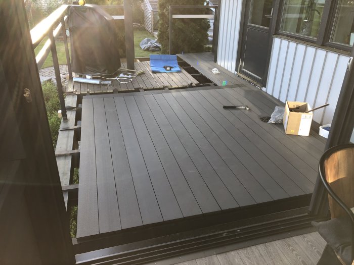 Pågående installation av mörk trall på en uteplats med verktyg och förpackningsmaterial utspridda runtom.