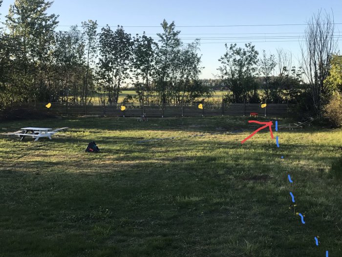 Trädgård med nyligen byggt staket, markeringar för elinstallation, murat rum med röd pil och blå streckad linje för kabeldragning.