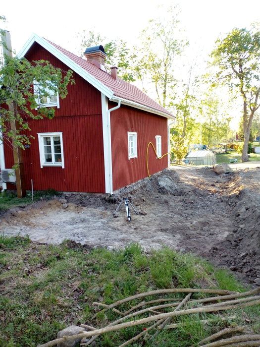 Röd stuga med pågående grävarbete bredvid för förberedelse inför gjutning.