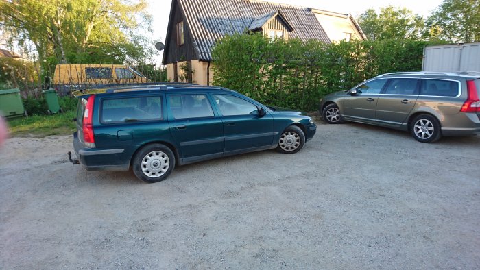 Två bilar parkerade mycket nära varandra på en grusplan med byggnader i bakgrunden.