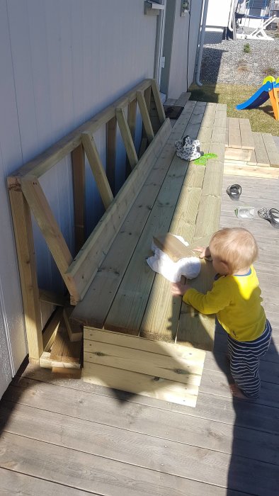 Ettåring står bredvid en hemmabyggd kombinerad trätrappa och sittbänk med förvaring på en altan.