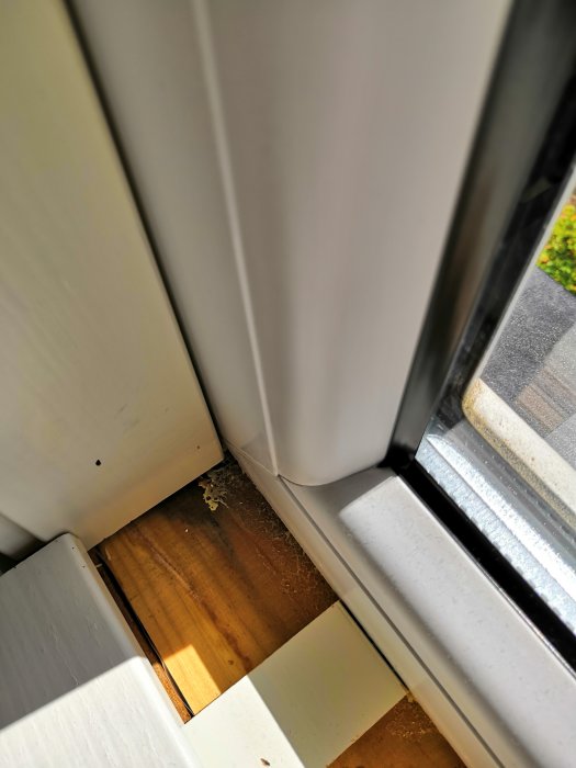 Invändig vy av ett fönsterhörn med grånad träyta och överflödigt fogskum vid fönsterblecken.