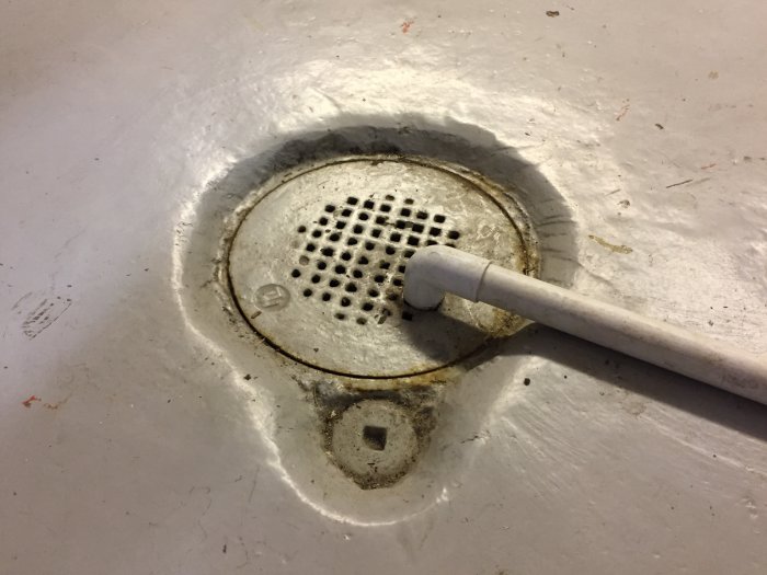 Golvbrunn med fall i ett garage, med avloppsröret ledande ner till den nedsänkta brunnen.