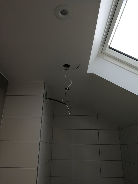 Ett badrum under renovering med klinkergolv, kaklade väggar och elledningar som hänger från taket.