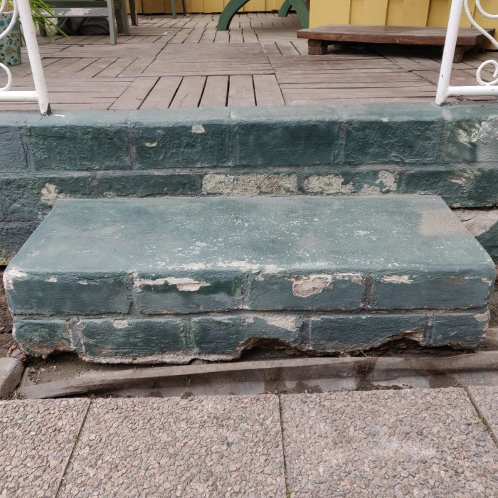 Altantrapp med släppt och flagande grönmålad yta, vittrade fogar och skador från rost och fukt.