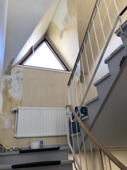 Renovering av trapp med delvis borttagen tapet och synligt gips på vägg och tak.