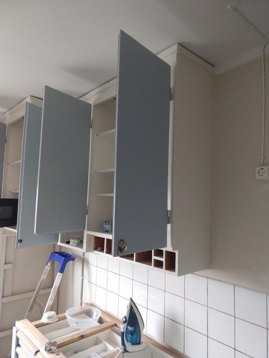 Kök under renovering med öppna överskåp, kaklad vägg och arbetsmaterial på bänk.