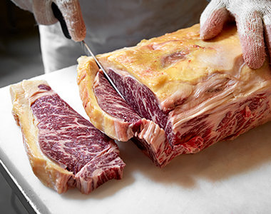 Hands skär i ett hängmörat köttstycke med mörk färg och riklig marmorering.