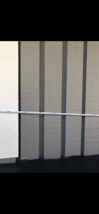 Vit garagevägg med vertikal träpanel och en meterstock för skalamätning.