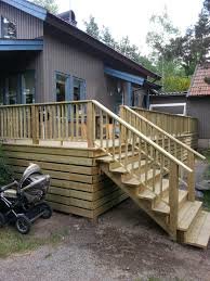 Träveranda med räcke och trappa vid en enfamiljshus, barnvagn i förgrunden.