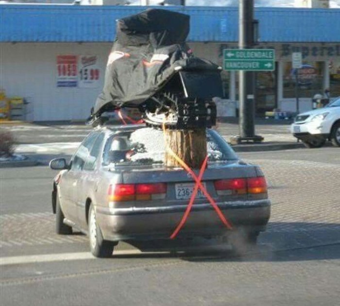 Bil överlastad med stort objekt fastsäkrat med spännband, otrygg transport på gata.