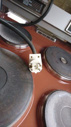 Gammal spis med fyra kokplattor och perilexkontakt ovanpå, tecken på användning och ålder syns.