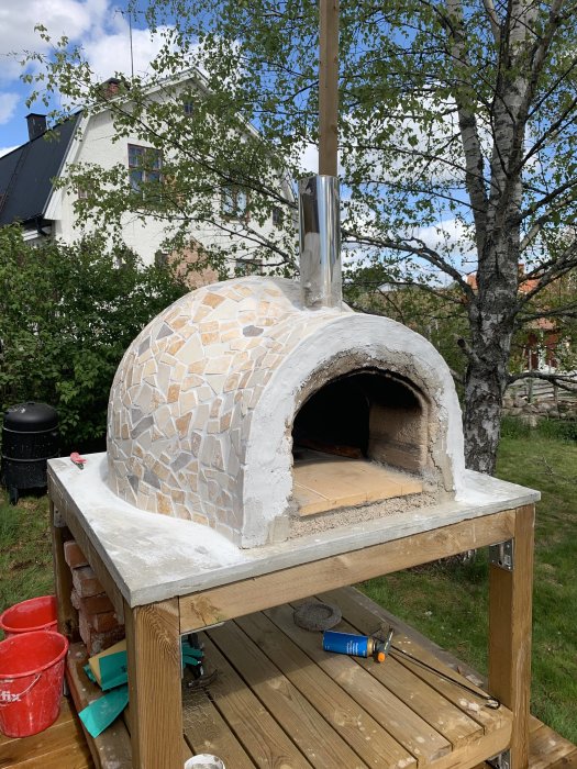 Nybyggd pizzaugn av sten med skorsten utomhus, placerad på trädäck.