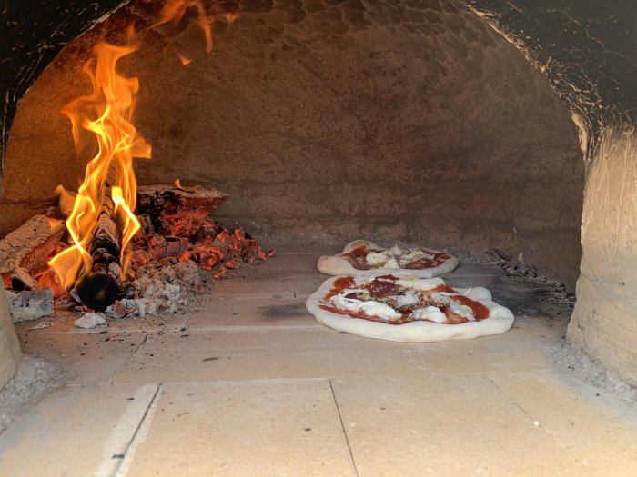 Tre pizzor bakas i en vedeldad ugn med synliga lågor och glödande kol.