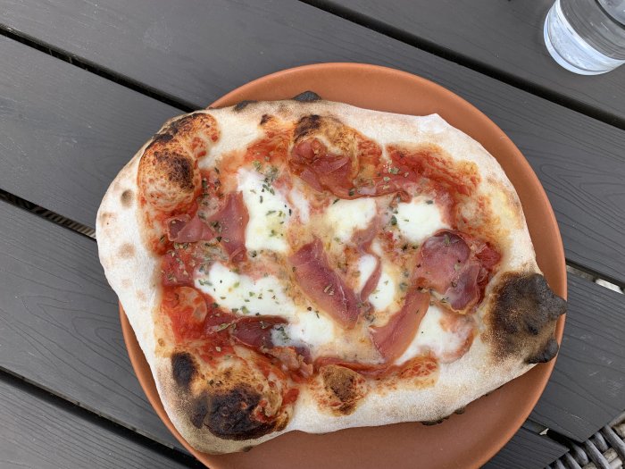 Nybakad pizza med tomat, ost och skinka på ett brunt fat ovanpå ett mörkt bord.