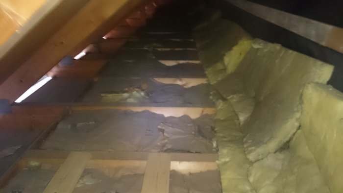 Bild på kallvinden i ett 70-talshus med sparsam isolering där gullfiber är uppträngt mot en vägg som tilläggsisolering.