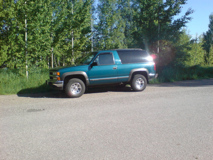 Teal SUV parked on the side of the road with trees in the background.