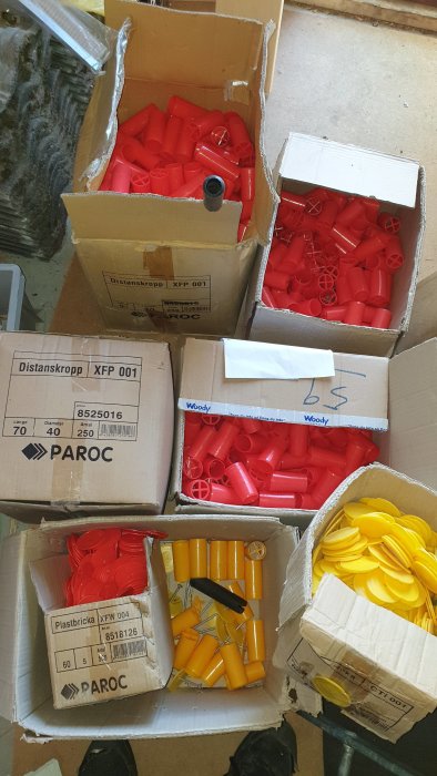 Kartonger med röda och gula distanshylsor och plastbrickor för isoleringsarbeten.
