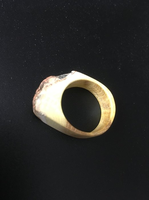 Handgjord ring i trä på en svart bakgrund, handarbete av lärling Jesper i miniatyrformat.