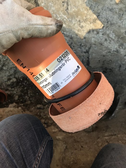 Hand håller i en PVC-rörskarv som ska anslutas till ett befintligt betongrör.