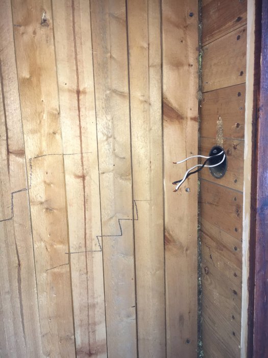 Gammal träpanelvägg i en hall från 1945 med spår av en dold struktur och utstickande elledningar från en urtagen brytare.