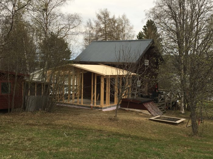Hus under renovering med råspont på ena sidan av taket, andra sidan ofärdig, omgivet av träd och gräs.