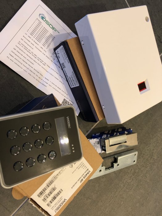 Oanvända säkerhetssystemdelar inkl kortläsare och elslutbleck i originalkartonger på golv.